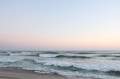 the ocean waves are rolling in and out of the water at sunset or dawn on an empty beach