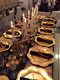 a long table is set with gold plates and place settings, candles in the middle