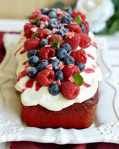 a red velvet cake with white frosting and berries on top is sitting on a plate