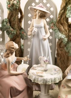 two figurines sitting at a table with tea cups and saucers on it