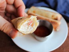 a person holding up a piece of food on a plate with dipping sauce in it