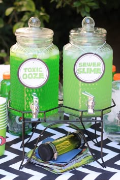 there are two jars with green liquid in them on top of a black and white table cloth