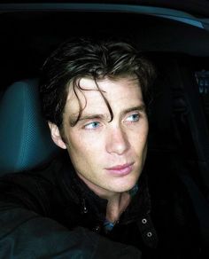 a man sitting in the back seat of a car with blue eyes and curly hair