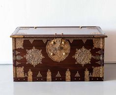 an ornate wooden box with gold decorations on the front and sides, sitting against a white wall