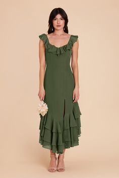 a woman wearing a green dress with ruffles on the side and a flower in her hand