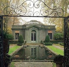 an old house with a pond in the middle of it and a wrought iron gate