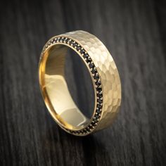 a gold wedding ring with black diamonds on it sitting on a wooden table in front of a dark background