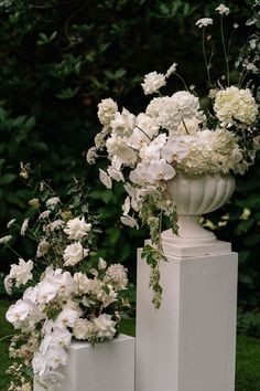 three white vases filled with flowers sitting on top of each other in the grass