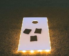 an illuminated cornhole board on the ground with pieces cut out to look like pillows