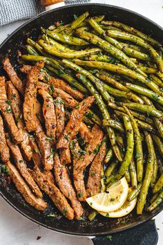 asparagus and steak in a skillet with lemon wedges on the side