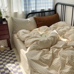 an unmade bed with a checkered comforter and pillows on it in front of a window