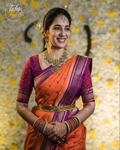 a woman in an orange and purple sari with gold jewelry on her neck smiling at the camera