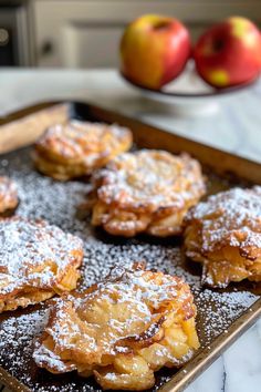 powdered sugar covered pastries on a baking sheet with apples in the back ground