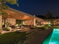 a house with a swimming pool in the middle of it at night, surrounded by greenery