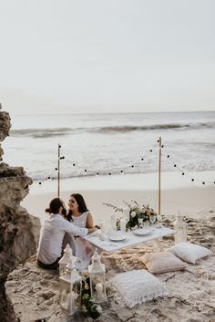 two people sitting at a table on the beach