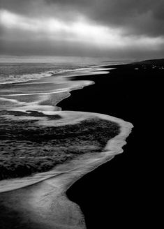 a black and white photo of the ocean with dark clouds in the sky above it