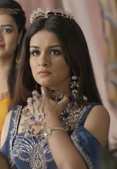 a woman wearing a tiara and jewelry in front of two mannequins