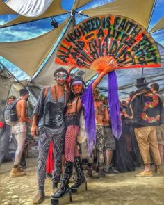 two people standing next to each other in front of a tent with an orange fan