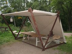 a wooden bench sitting under a tent on top of a field