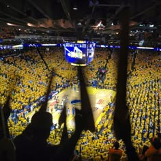 a crowd of people watching a basketball game in a large arena with yellow shirts on the floor