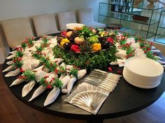 the table is set for christmas dinner with white plates and silverware on it, along with holiday decorations