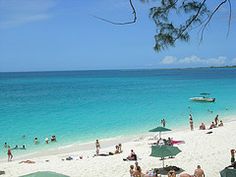 many people are on the beach with umbrellas and boats in the water behind them