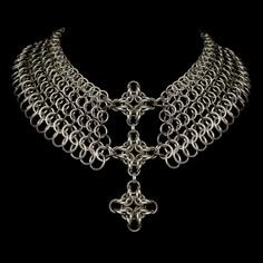 a silver necklace on a black background with an ornate design in the center and two chains attached to it