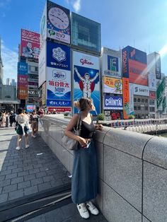 a woman leaning against a wall in front of billboards with advertisements on the side