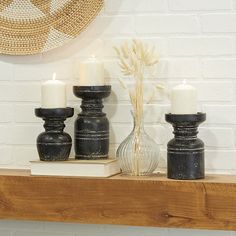 three candles are sitting on a shelf next to two vases and a straw hat