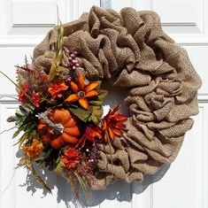 a burlap wreath with fall flowers and leaves on the side of a white door