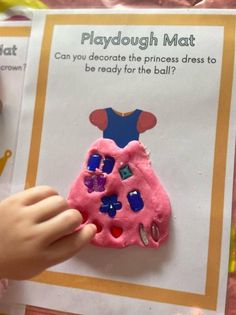 a child is holding a playdough mat in front of an activity book with instructions on how to decorate the princess dress