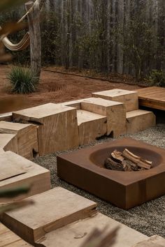 an outdoor fire pit surrounded by wooden steps and benches in the background is a wooded area