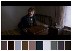 a man in a suit and tie sitting on a bed next to a suitcase with color swatches