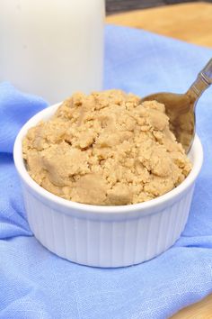 a white bowl filled with oatmeal next to a glass of milk on a blue cloth