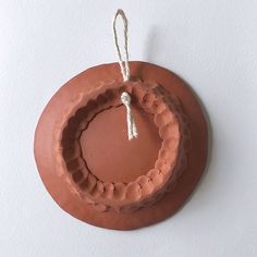 a clay ornament hanging from a string on a white wall with a tag attached to it