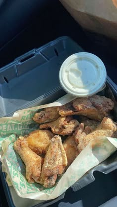 chicken wings and dipping sauce in a plastic container on the back seat of a car