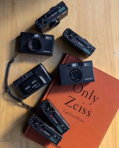 four cameras sitting on top of an orange book with the words only zeiss written in it