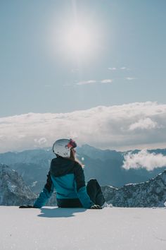 a person sitting on top of a snow covered slope with mountains in the back ground