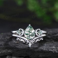 a white gold ring with green stones and leaves on it, sitting on a piece of wood