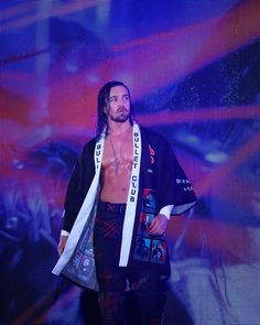 a man with no shirt on standing in front of a screen wearing a scarf and holding a bag