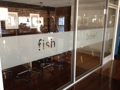 an office with glass walls that says fish on the front and back windows, along with wooden flooring