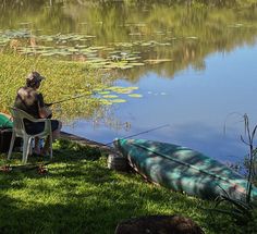 a man sitting in a chair next to a body of water with a fishing rod