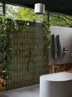 a bathroom with green tiles and plants on the shower wall, along with a round bathtub