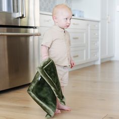 a small child standing on the floor with a towel in his hand and an oven behind him