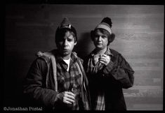 two young men standing next to each other in front of a wooden wall wearing hats