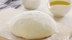 a ball of bread sitting on top of a wooden cutting board next to a bowl