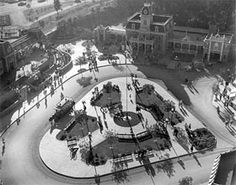 an aerial view of a park with benches and trees in the center, surrounded by buildings