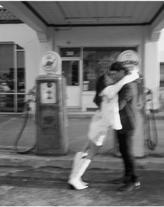 a man and woman kissing in front of a gas station