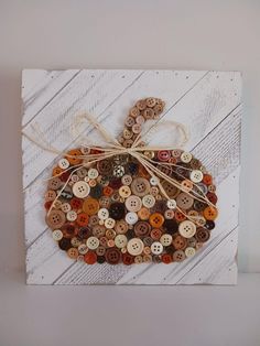 a pumpkin made out of buttons sitting on top of a piece of white wooden plank