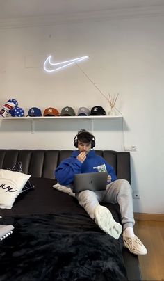 a man sitting on top of a bed with headphones and using a laptop computer